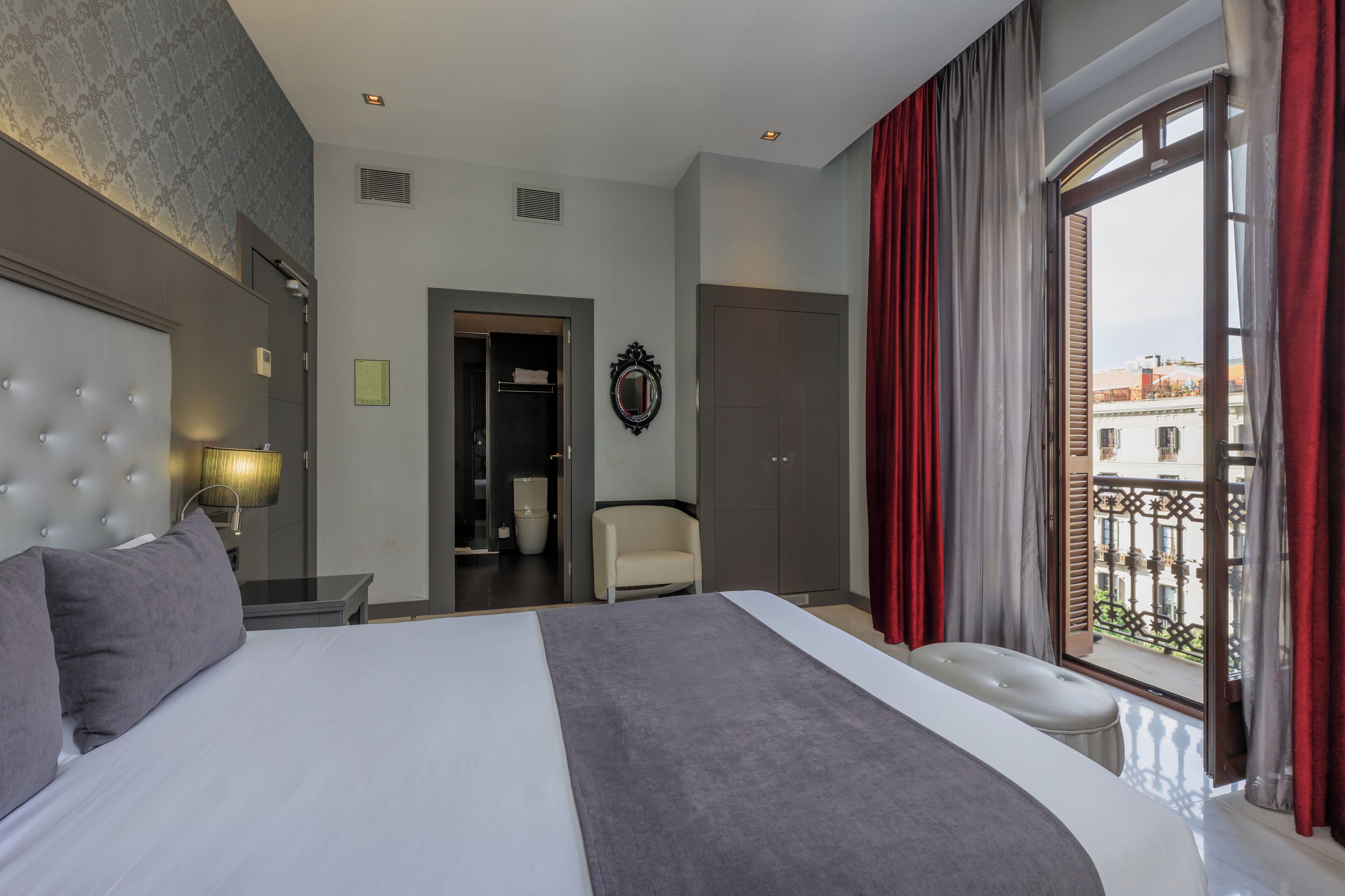 Ett modernt hotellrum med en stor säng, en sittgrupp, en garderob och utsikt över staden från balkongen.