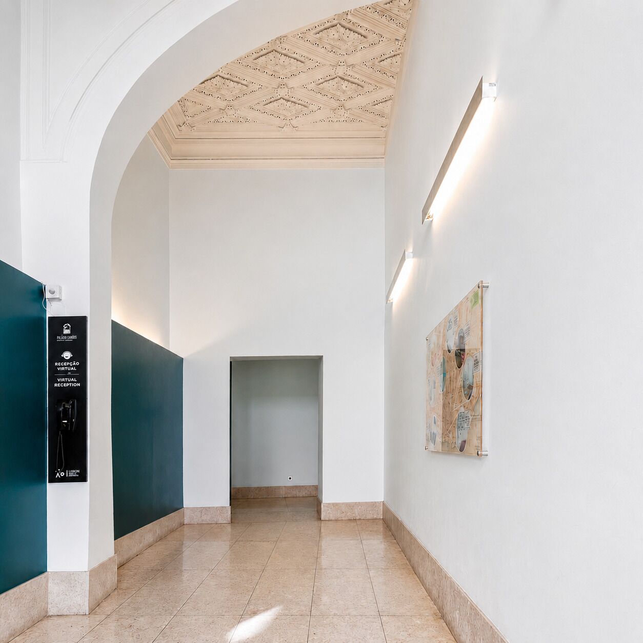Un pasillo con mostrador de recepción, una obra de arte en la pared y un techo con diseño geométrico.
