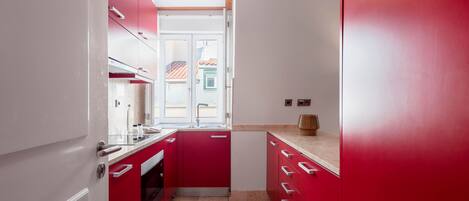 A narrow kitchen with red cabinets, a white countertop, and a pendant light.