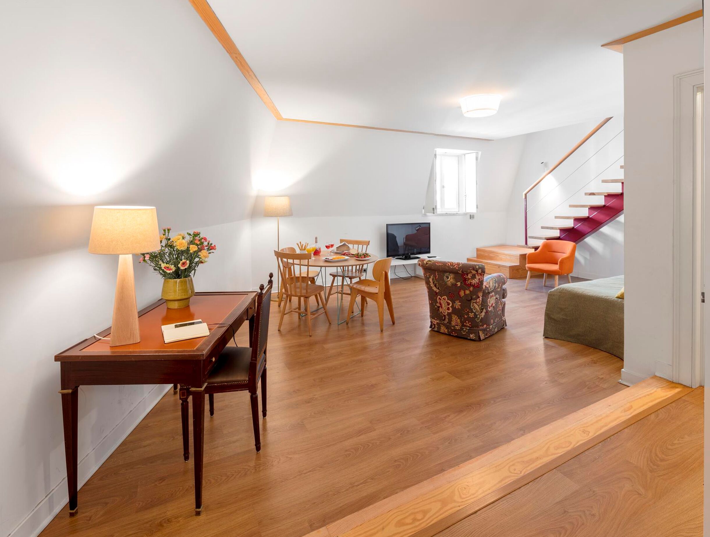 A modern living room with a dining area, wooden flooring, a TV, and a staircase.