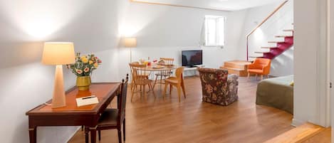 A modern living room with a dining area, wooden flooring, a TV, and a staircase.