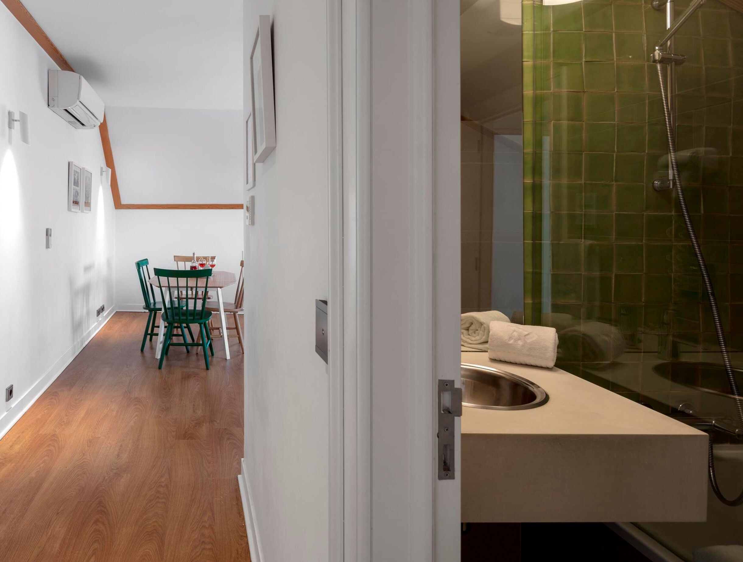 A hallway with a dining area, a shower with green tiles, and a sink.