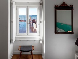 Quarto com vista para um terraço, uma cadeira de madeira e um espelho na parede.