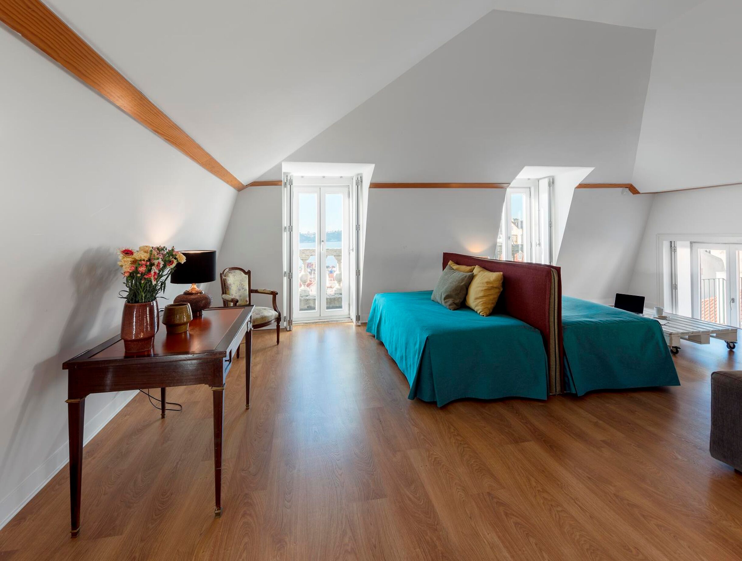 Ein Schlafzimmer mit einem Bett, einem Schreibtisch und einem Stuhl. Ein Fenster und eine Tür führen nach draußen.