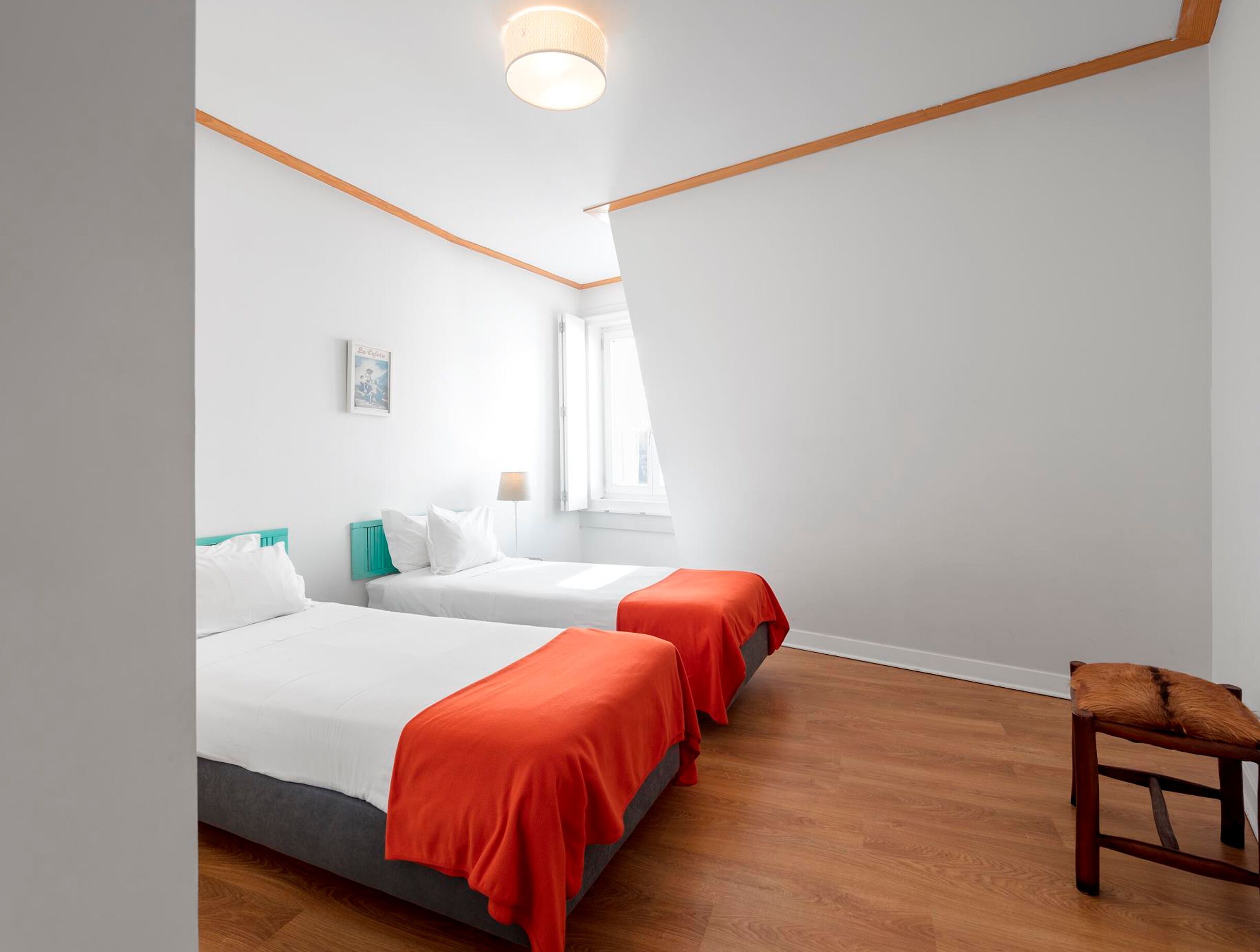 Habitación de hotel con dos camas, piso de madera, una ventana y una pequeña silla.