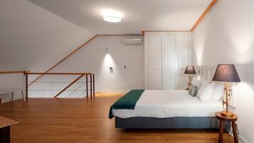Un dormitorio con cama, lámparas de noche, suelo de madera, un armario blanco y una escalera.