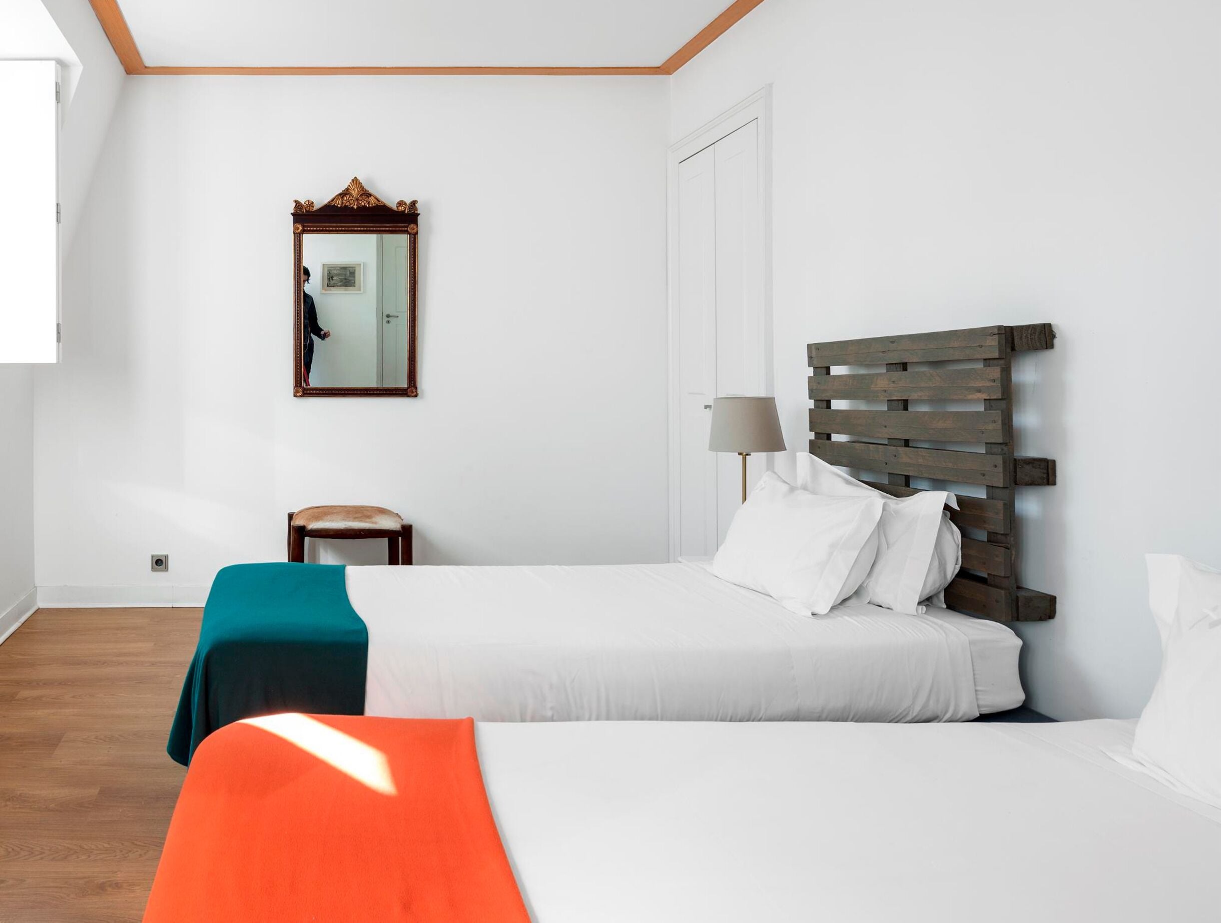 A bedroom with a bed, a chair, a small table, a lamp, and a mirror on the wall.