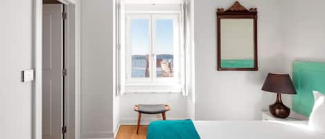 A hotel room with a bed, a window with a view, a mirror, and a nightstand.