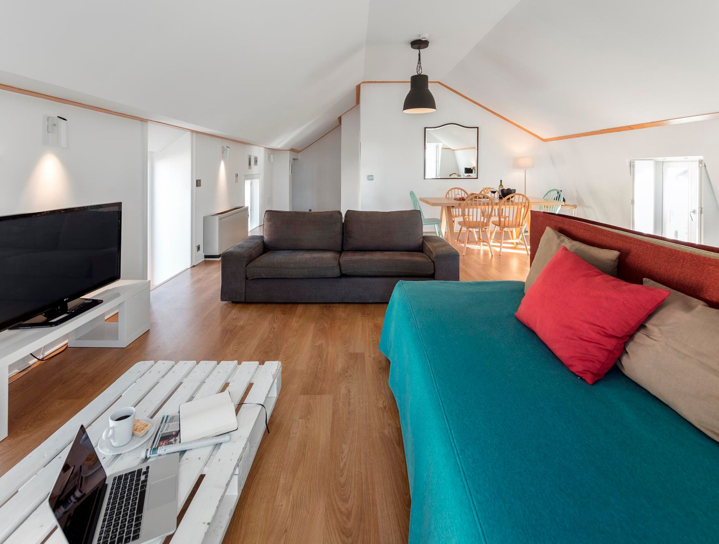 Una sala moderna con televisor, sofá y mesa de centro, un comedor con sillas y una cocina al fondo.