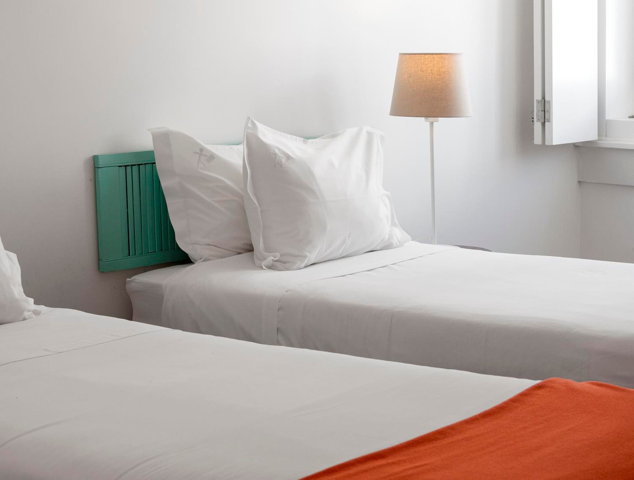 A hotel room with two beds, a green headboard, a floor lamp, and a window.