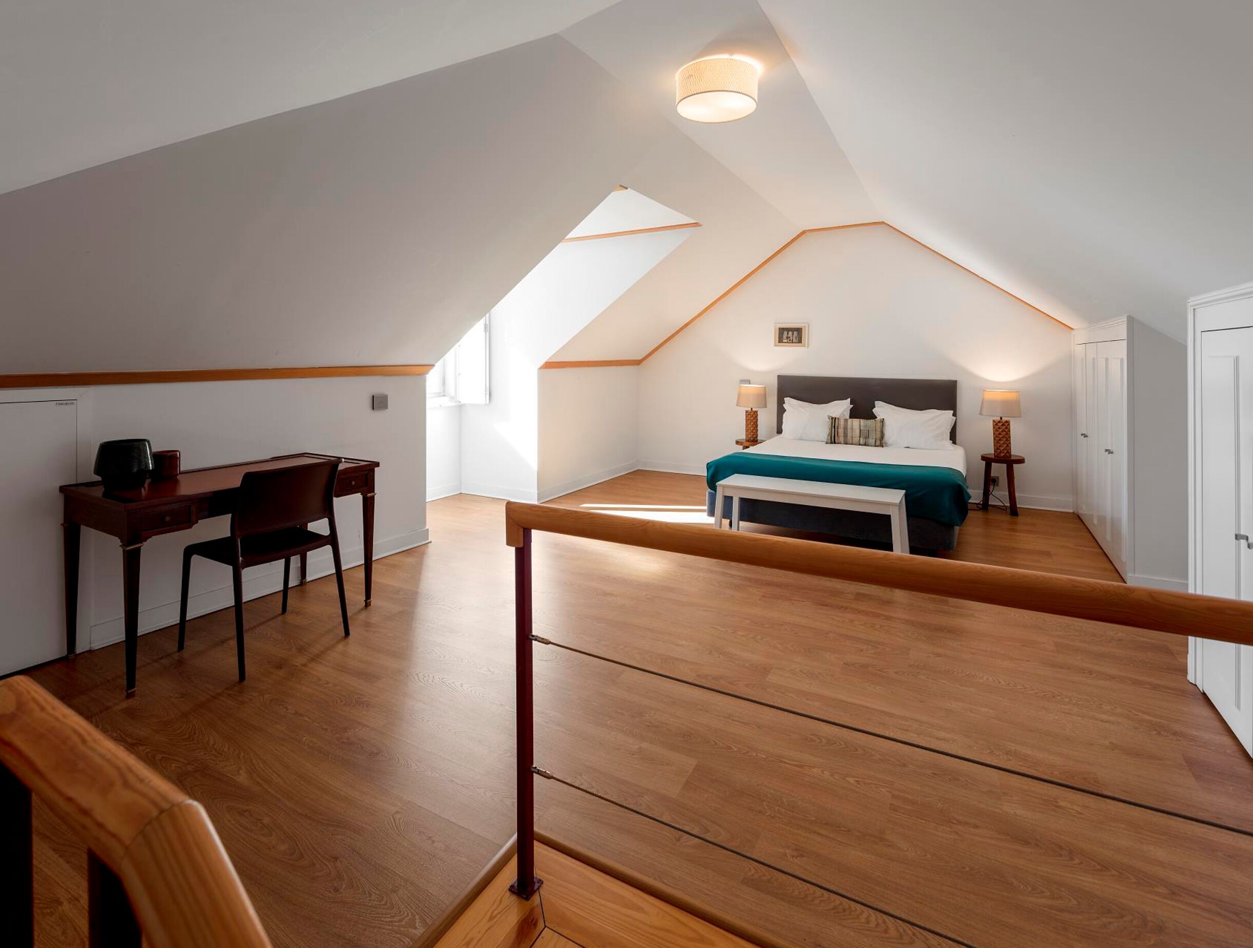 A bedroom with a bed, bedside table, lamp, and a desk with chair.