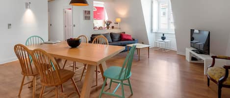 En moderne opholdsstue med spiseplads, sofa, fjernsyn og et køkken i baggrunden.