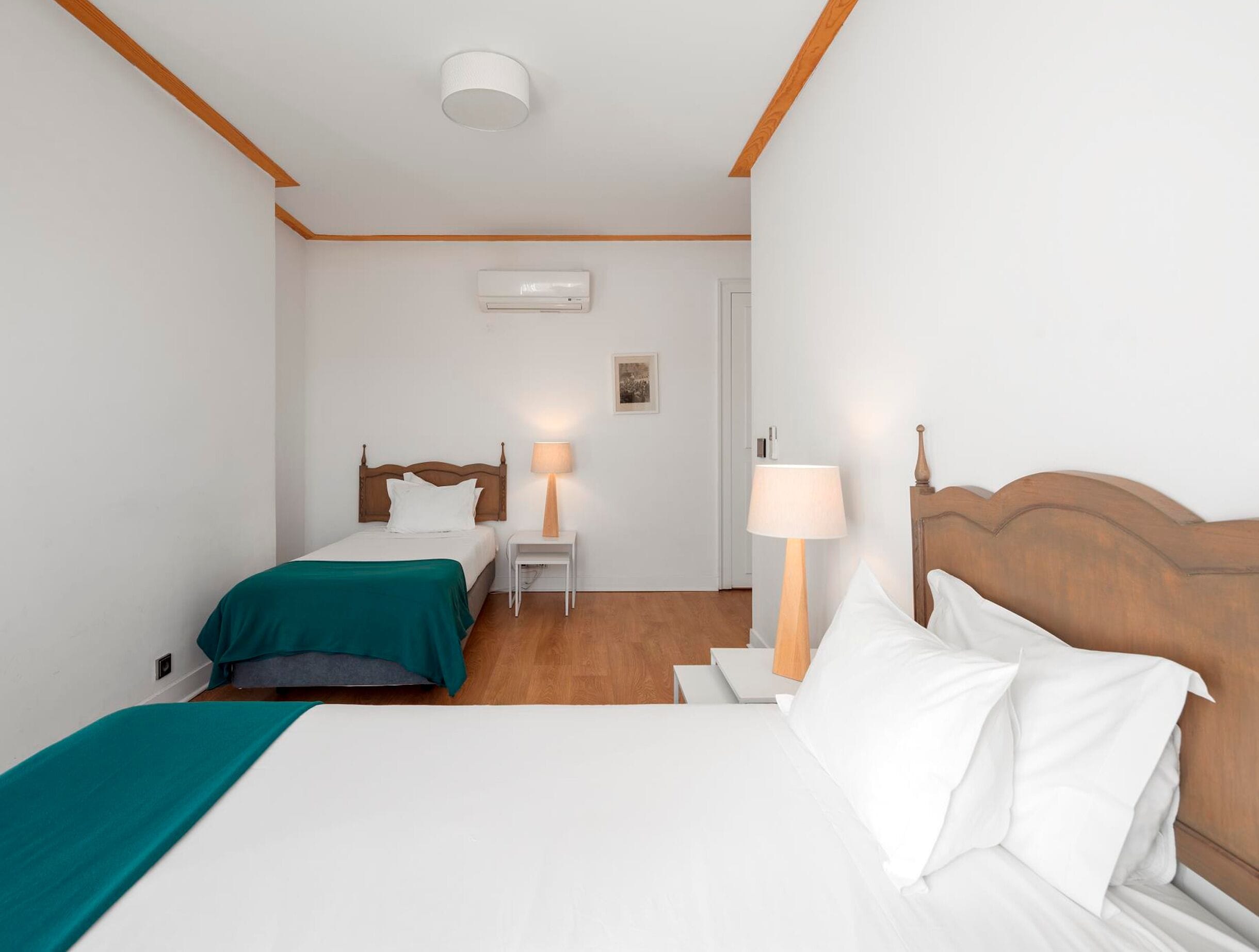 Una habitación de hotel con dos camas, una lámpara de techo, un equipo de aire acondicionado y una mesita de noche con lámpara.