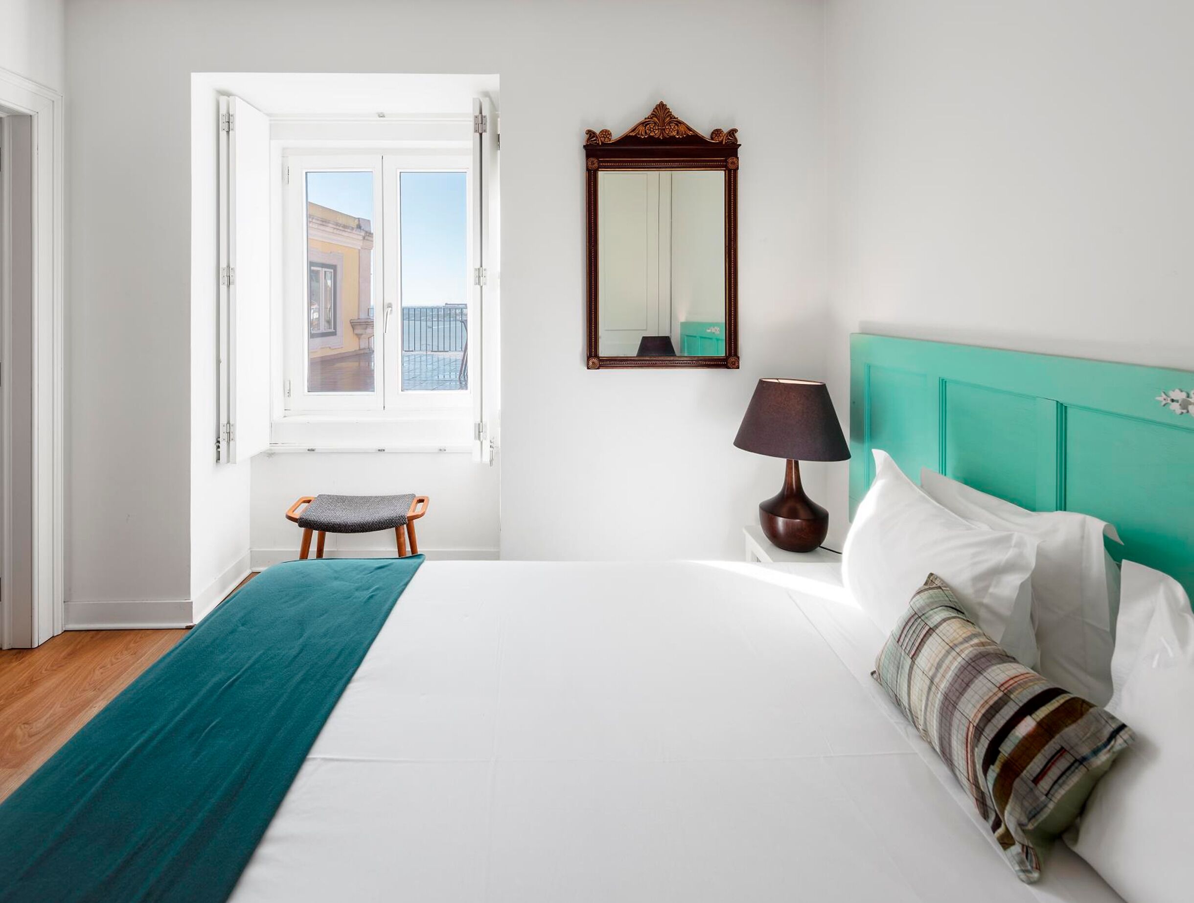 A bedroom with a bed, a window, a chair, a lamp, and a mirror.
