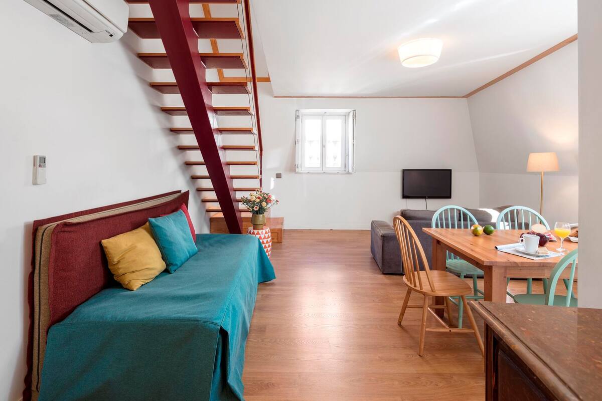 A room with a sofa, a dining table, chairs, a TV, and a staircase.