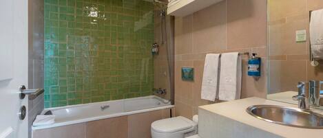 Un baño con ducha revestida de azulejos verdes, una bañera blanca, inodoro y lavamanos con espejo.