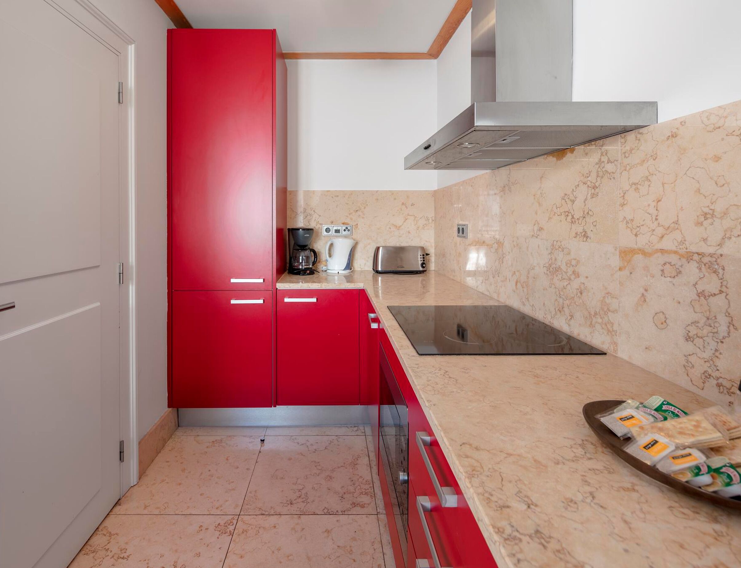 A kitchen with red cabinets, a stainless steel range hood, a countertop with a toaster, and a tray of bread.