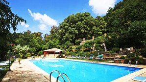 A swimming pool with a tiled deck, lounge chairs, and a small building in a lush, green environment. - Torre di Renda (Piazza Armerina)