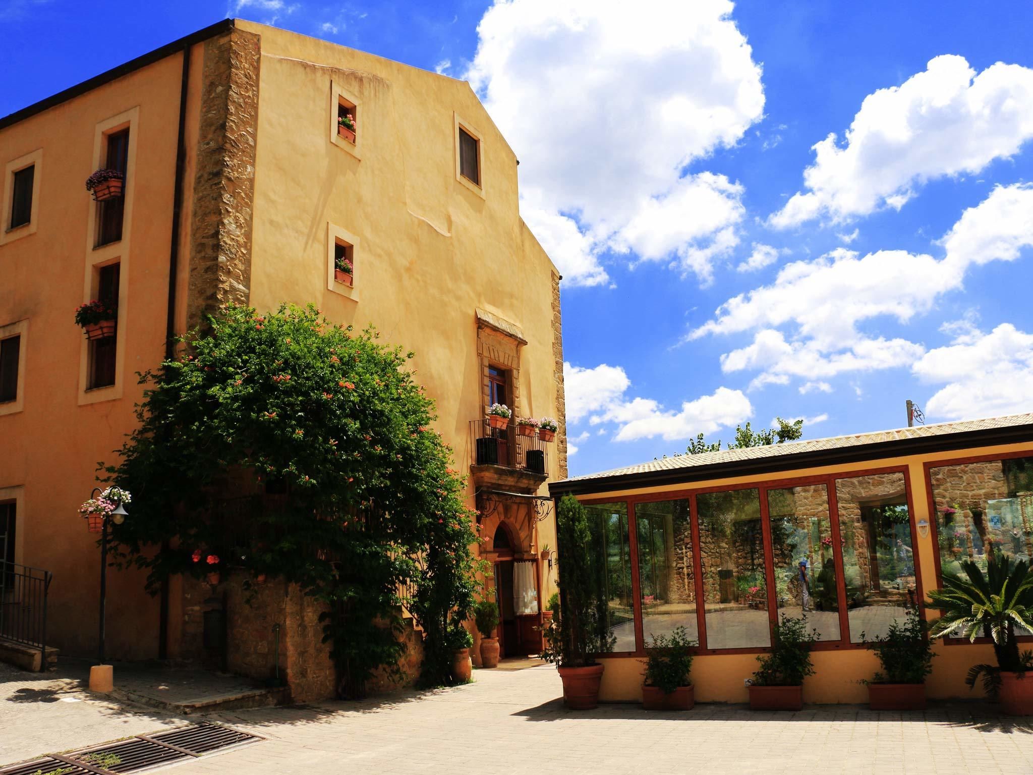 A building with a yellow facade, large windows, and potted plants.