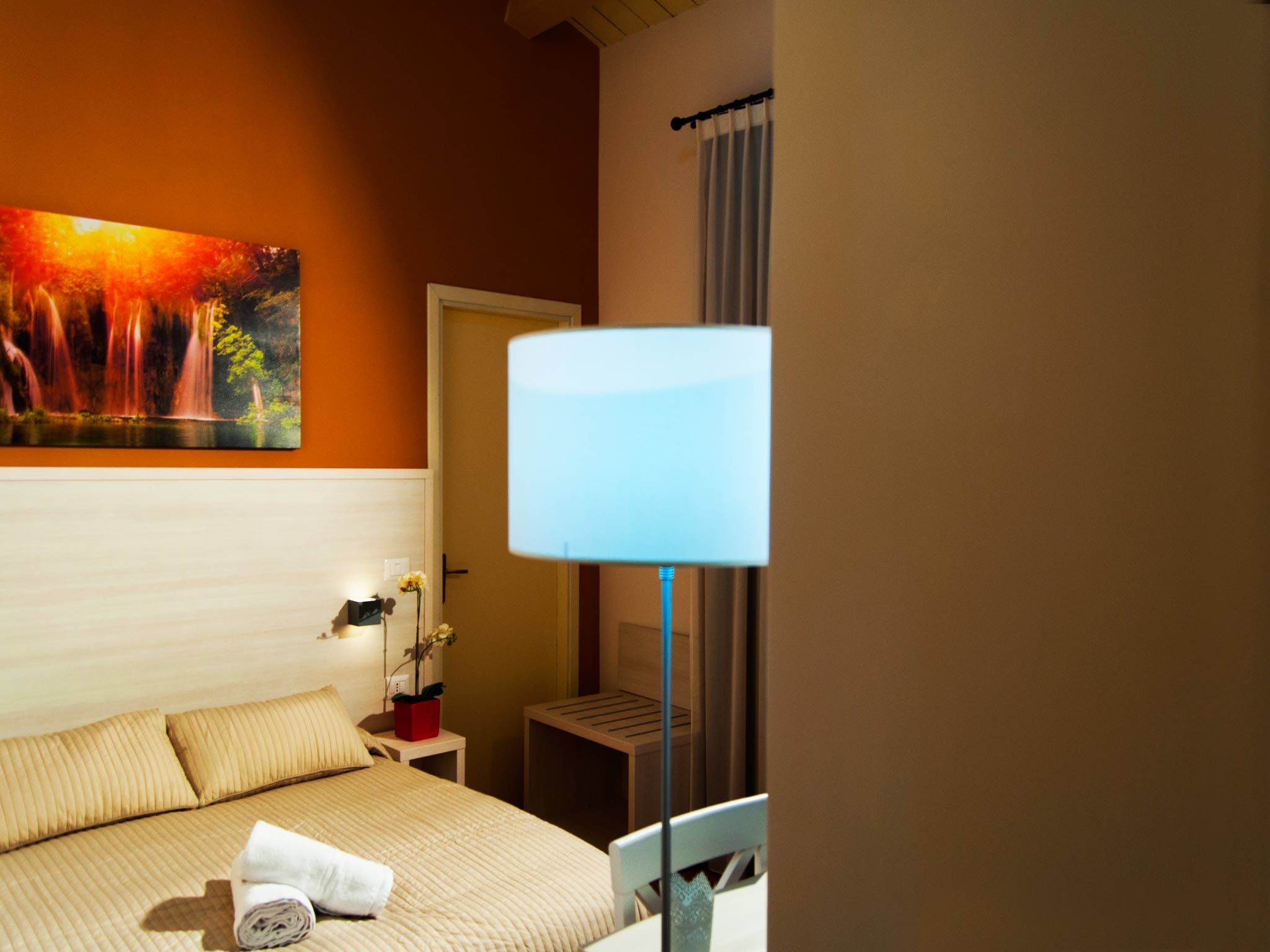 A hotel room with a bed, a nightstand, a lamp, and a painting on the wall.