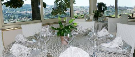 Une table à manger dressée pour six personnes, avec vue sur le paysage urbain à travers de grandes fenêtres.