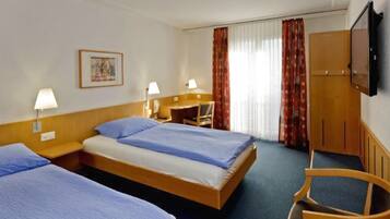 Een hotelkamer met twee eenpersoonsbedden, een bureau, een stoel, een televisie en een raam met gordijnen.