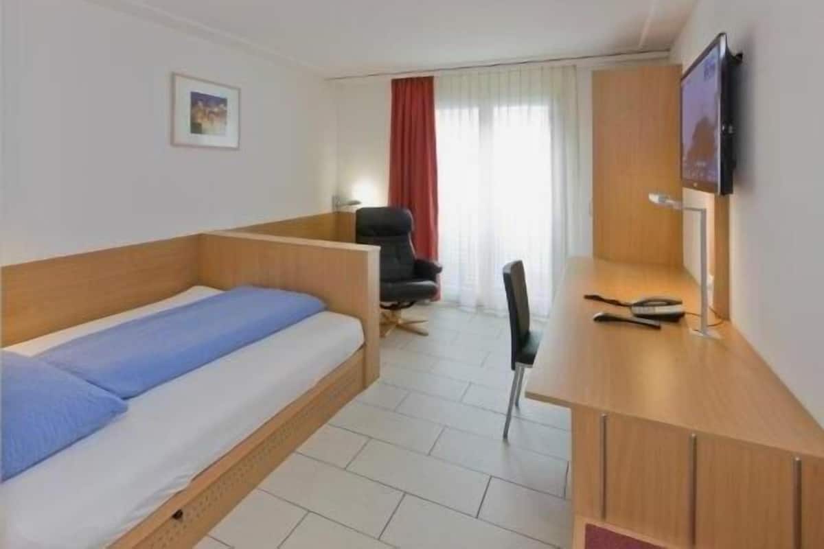 Habitación de hotel pequeña con una cama individual, un escritorio, una silla y un televisor.