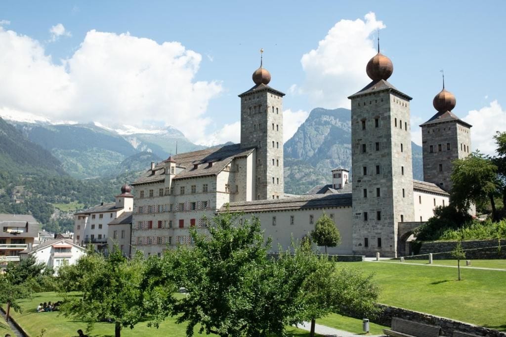 Un edificio histórico con múltiples torres y cúpulas, rodeado de exuberante vegetación y montañas.