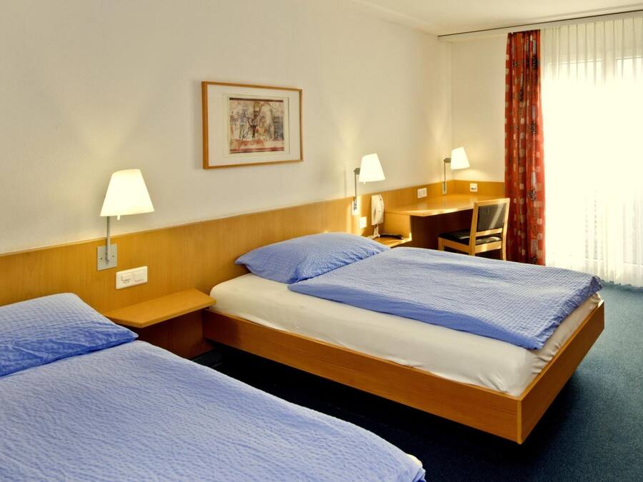 Una habitación de hotel con dos camas individuales, un escritorio, una silla y una ventana con cortinas.
