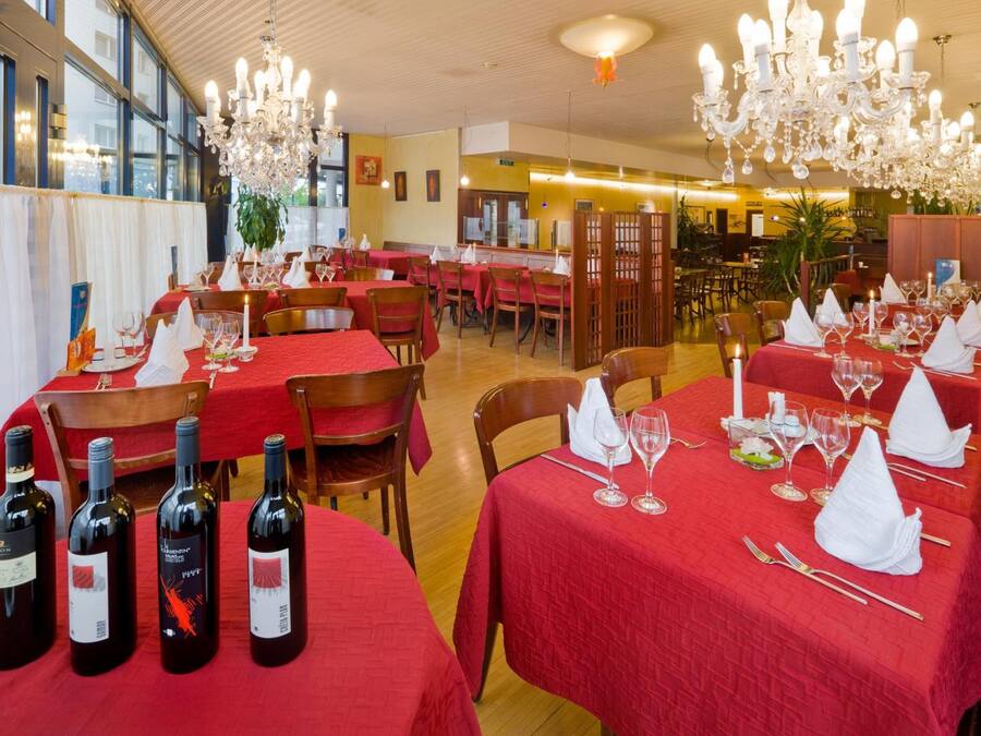 Un restaurante con mesas dispuestas para comer, con manteles rojos y botellas de vino.