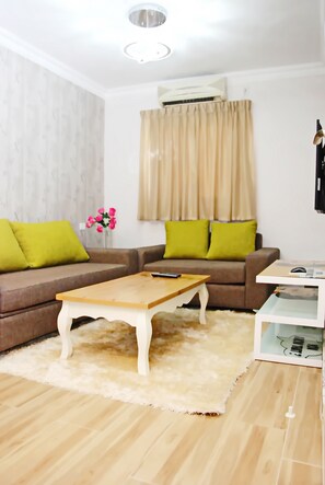 Ein modernes Wohnzimmer mit einem braunen Ecksofa, einem Holztisch, einem flauschigen weißen Teppich und einer weißen Klimaanlage.