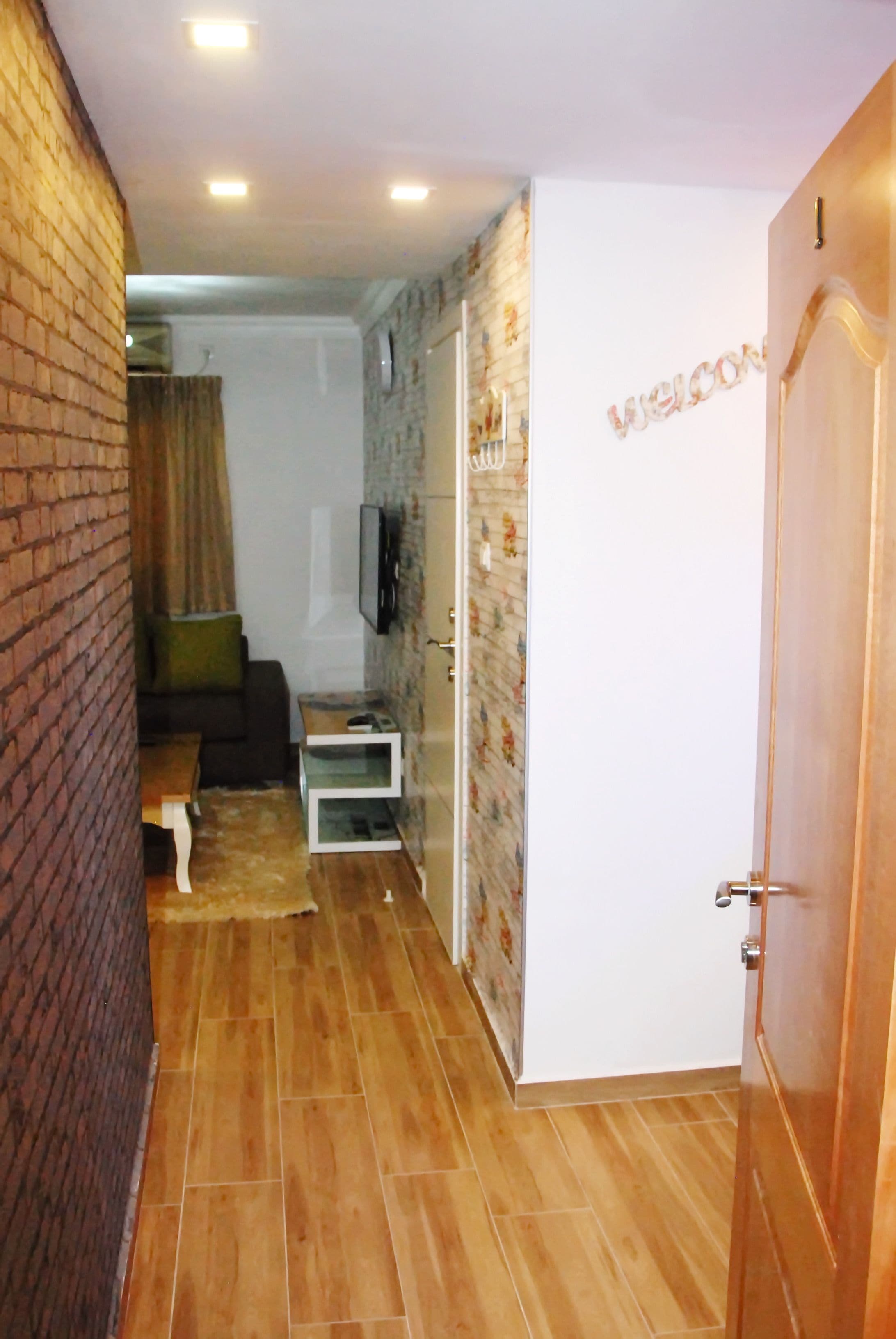 Un couloir étroit avec un plancher en bois, un mur de briques d’un côté et une porte blanche de l’autre.