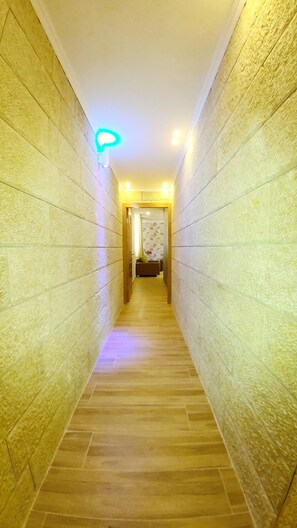 Ein schmaler Flur mit strukturierter Wandgestaltung und Holzboden, der zu einem Raum mit einer Couch und blumigem Wandpapier führt.