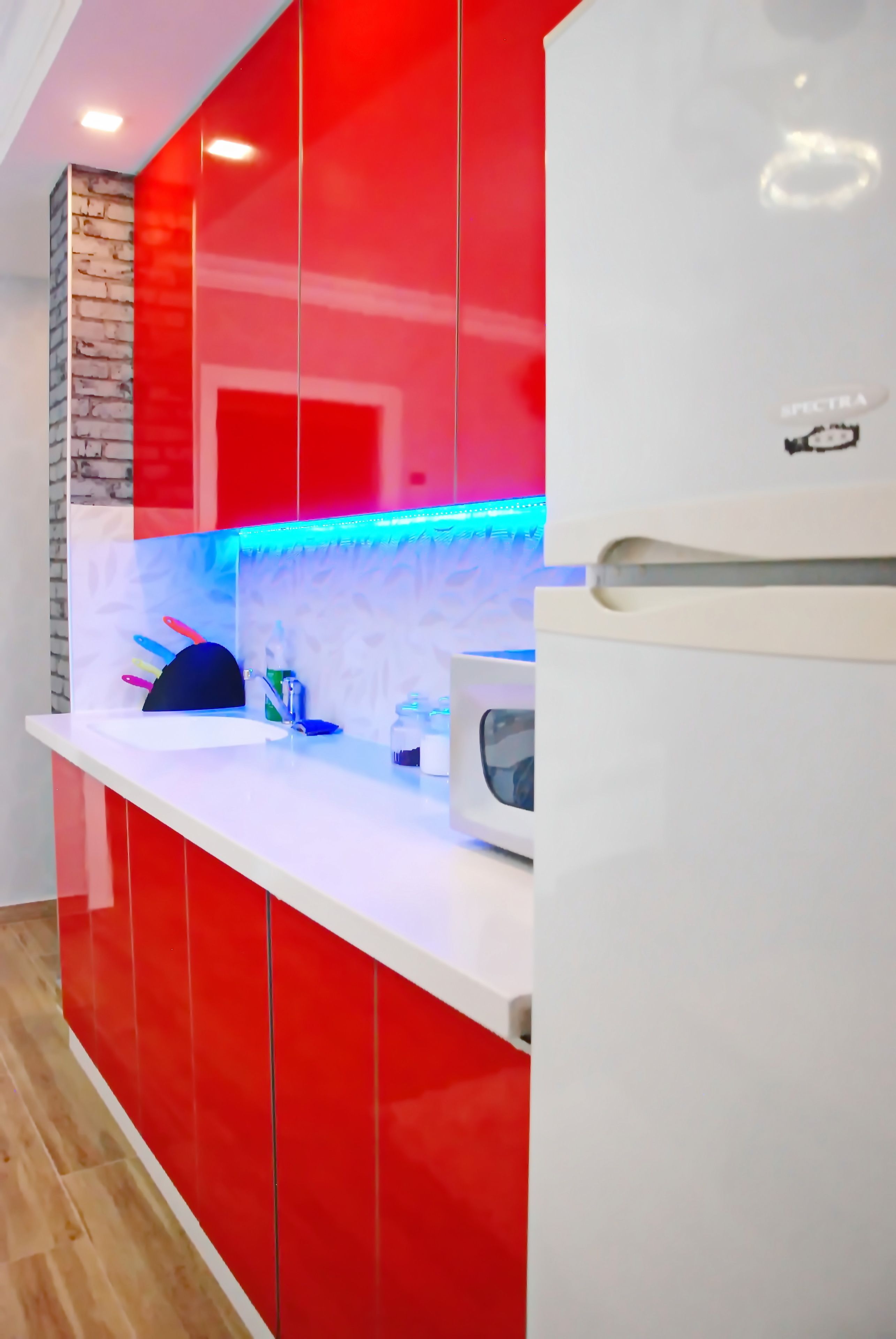 A modern kitchen with red cabinetry, a white countertop, and a built-in microwave.