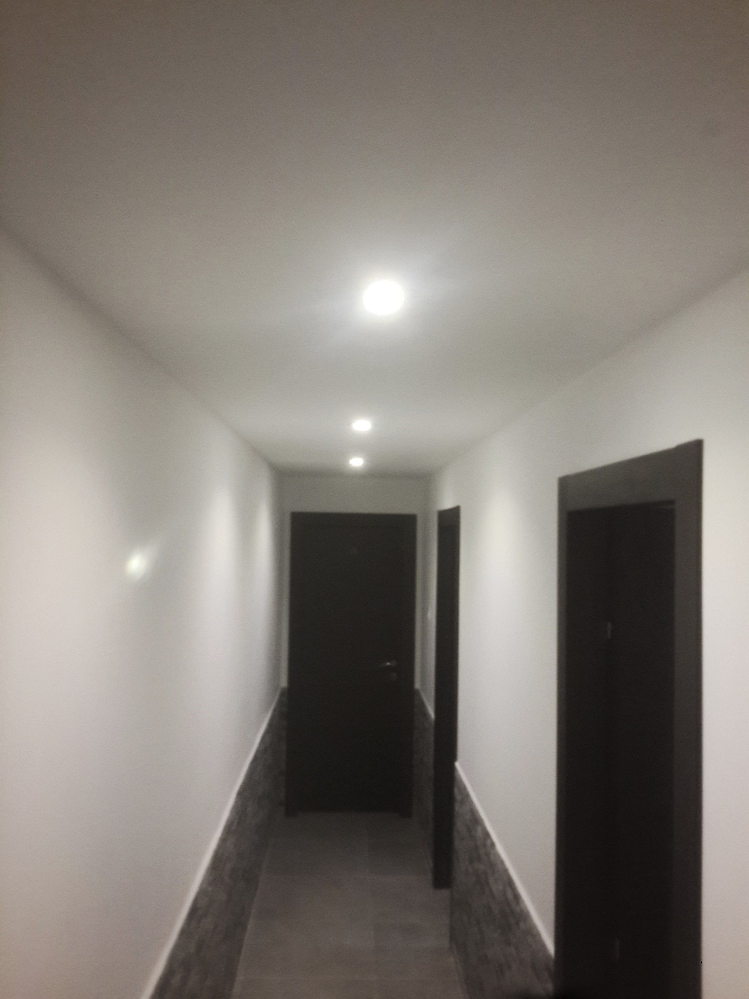 Ein schmaler, schwach beleuchteter Gang mit einer dunklen Tür am Ende und einer Leuchte an der Decke.