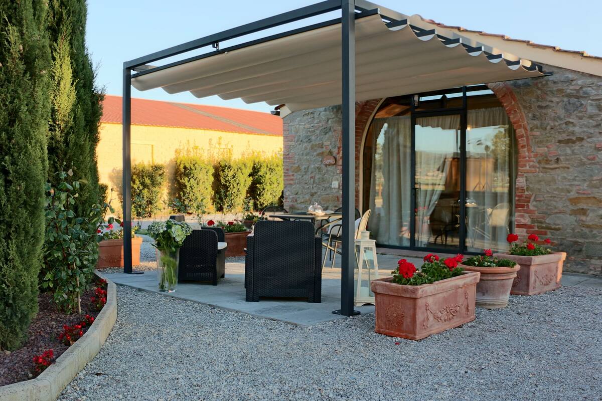 Un patio couvert avec des meubles d’extérieur, des plantes en pot et un bâtiment en pierre en arrière-plan.