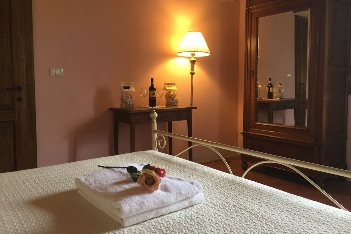 Un lit bien fait, avec une serviette pliée et une rose, une table de chevet avec une lampe et un miroir.