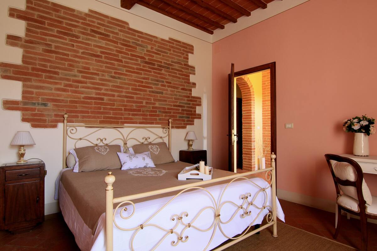 Une chambre avec un mur en briques, un lit avec une tête de lit, une table de chevet, un bureau et une chaise.
