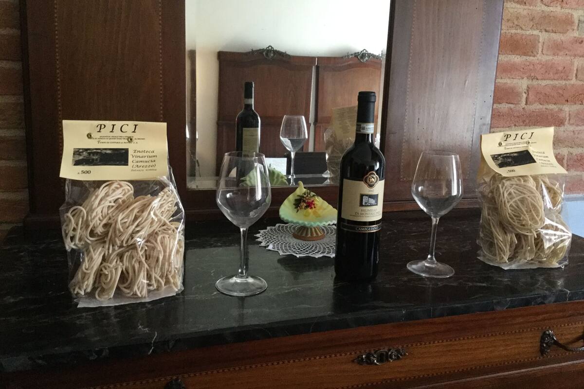 Une table avec deux paquets de pâtes PICI, une bouteille de vin Brunello di Montalcino et deux verres à vin vides.