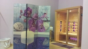 Une pièce comprenant un grand paravent décoratif à plusieurs panneaux représentant un motif d’orchidée, un sauna en bois et une chaise blanche.