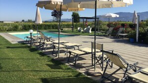 Un espace aménagé au bord de la piscine, avec des chaises longues et des parasols, une piscine et une vue sur les montagnes.