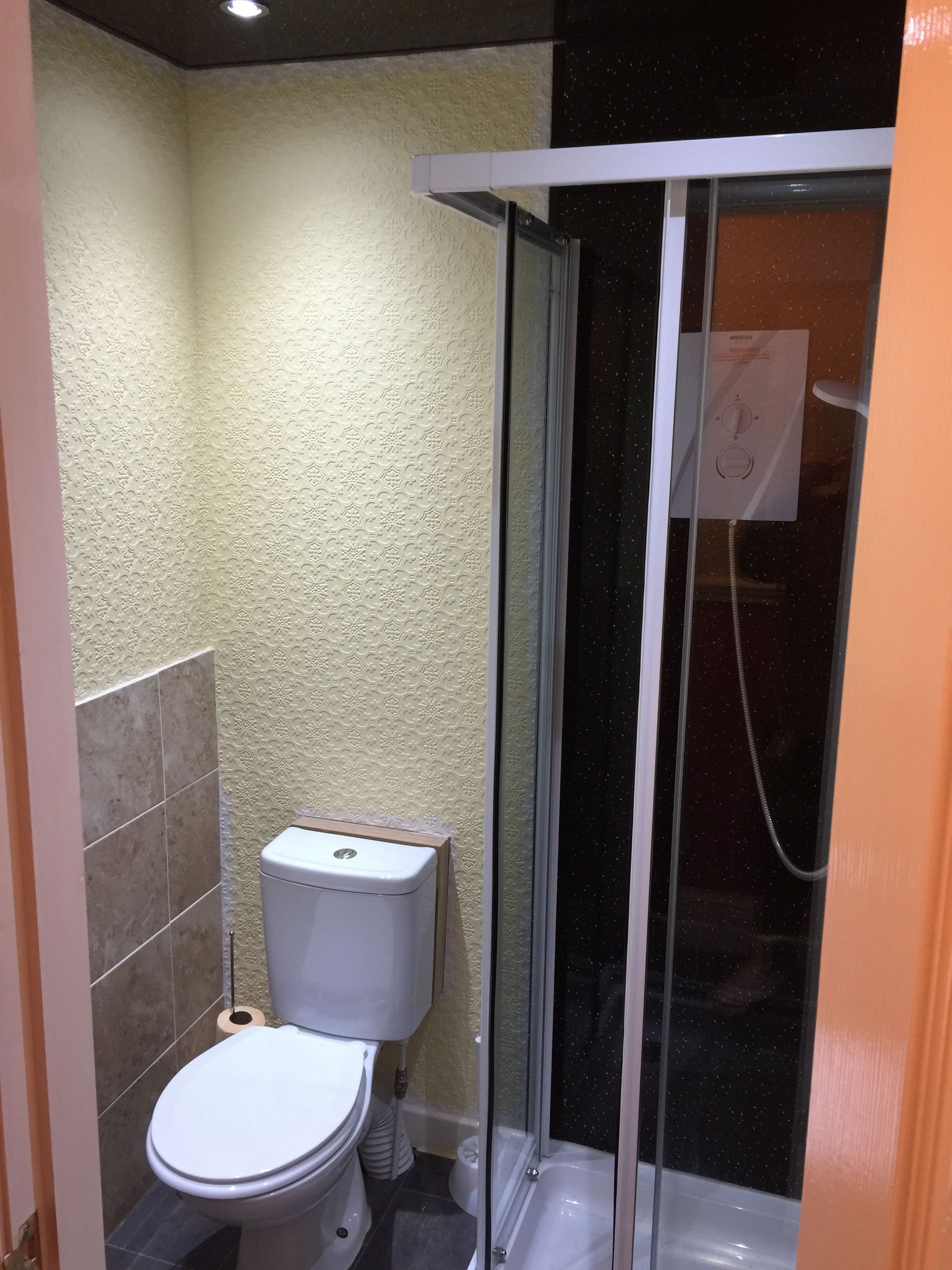 A bathroom with a toilet, a shower enclosure, and a wall with a textured pattern.