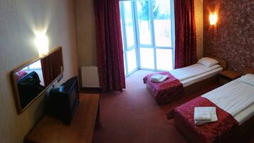 A hotel room with two single beds, a TV, a radiator, and a window with curtains.
