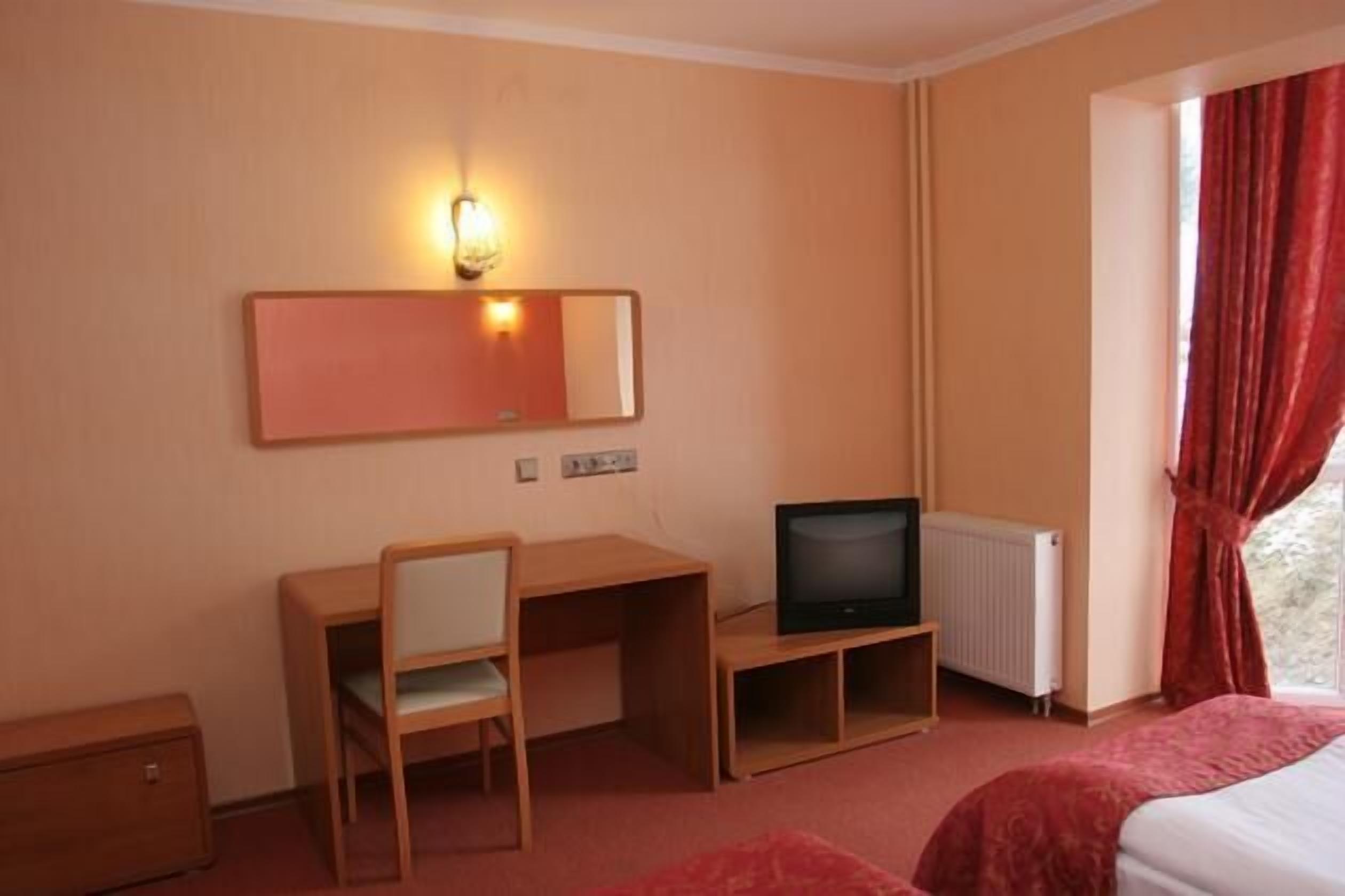 Une chambre d’hôtel avec un bureau en bois, une télévision, un lit et une fenêtre avec des rideaux rouges.