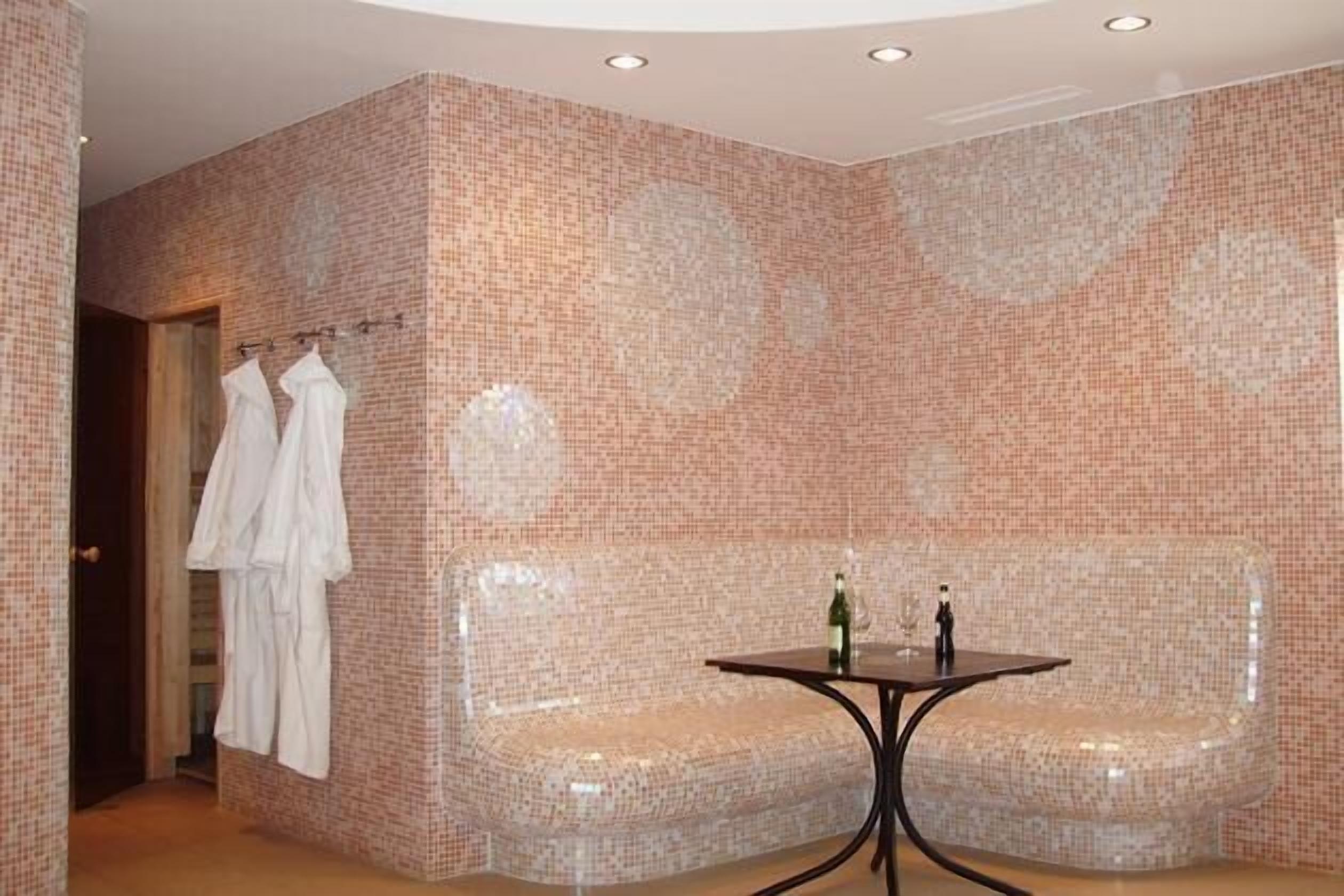 Une salle de bain aux murs recouverts de mosaïques, avec un banc et une table sur laquelle sont posées des bouteilles.