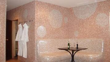 Une salle de bain aux murs recouverts de mosaïques, avec un banc et une table sur laquelle sont posées des bouteilles.