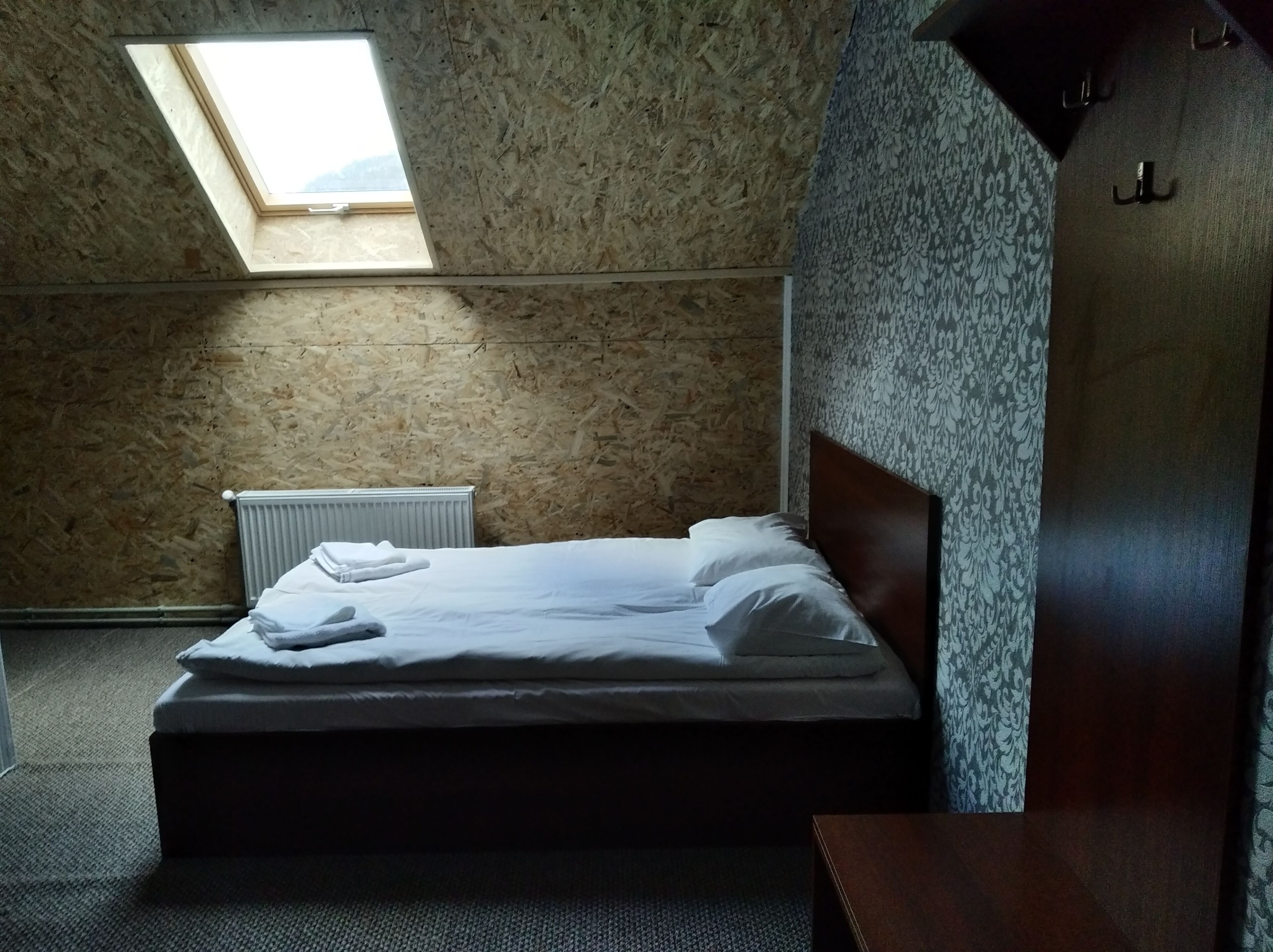 A bedroom with a sloped ceiling, a skylight, a radiator, and a bed with white linens.