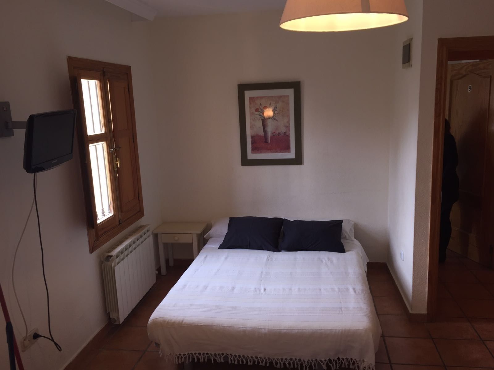 Camera da letto con un letto, un comodino, una TV a parete, una finestra e una porta.