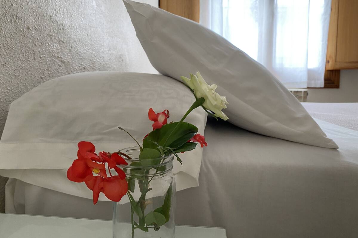 A room with a bed, a white pillow, and a vase with flowers.