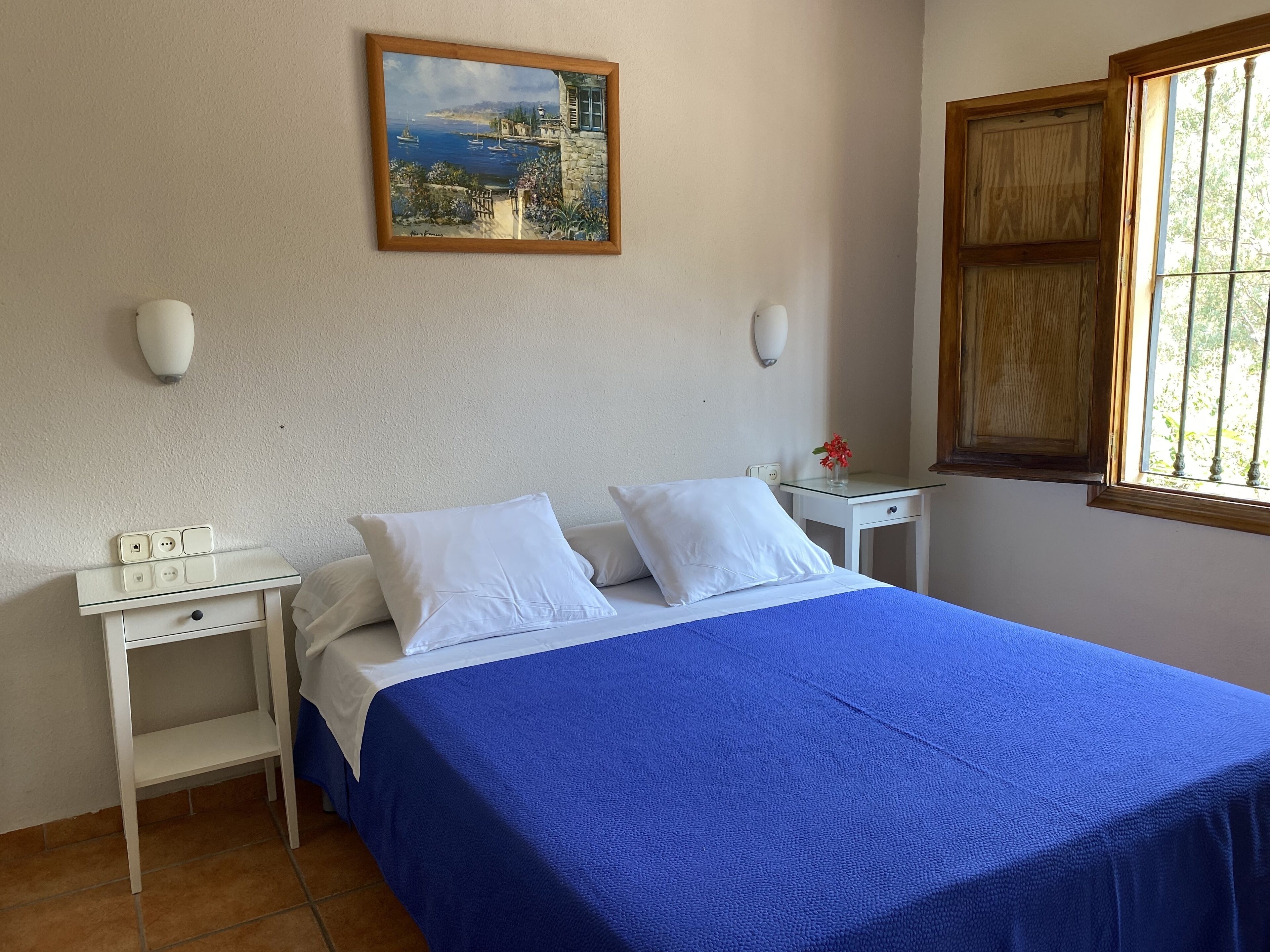 A bedroom with a bed, white nightstands, a painting, and a window.